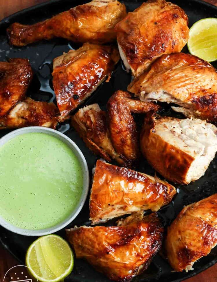 Roasted Peruvian chicken pieces served on a black platter with green sauce and lime wedges.