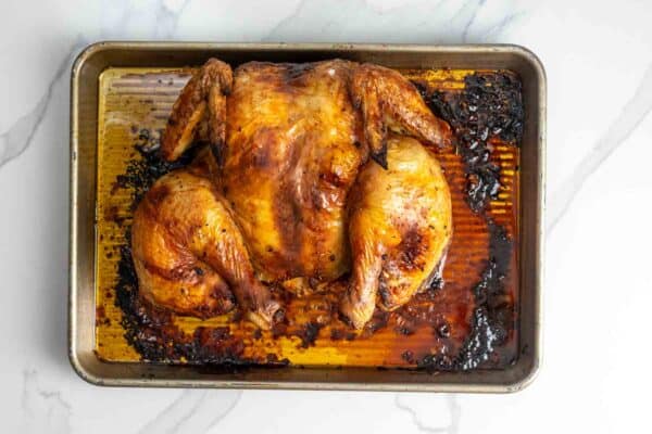 Whole roasted Peruvian chicken on a sheet pan with browned skin and pan juices.