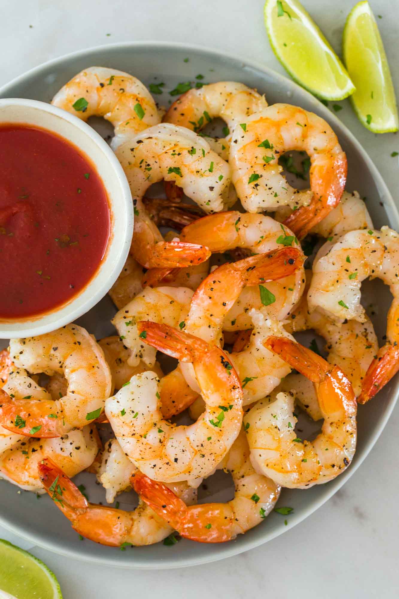 Overhead shot of perfectly cooked shrimp on a plate with a dip on the side, and wedges of lime