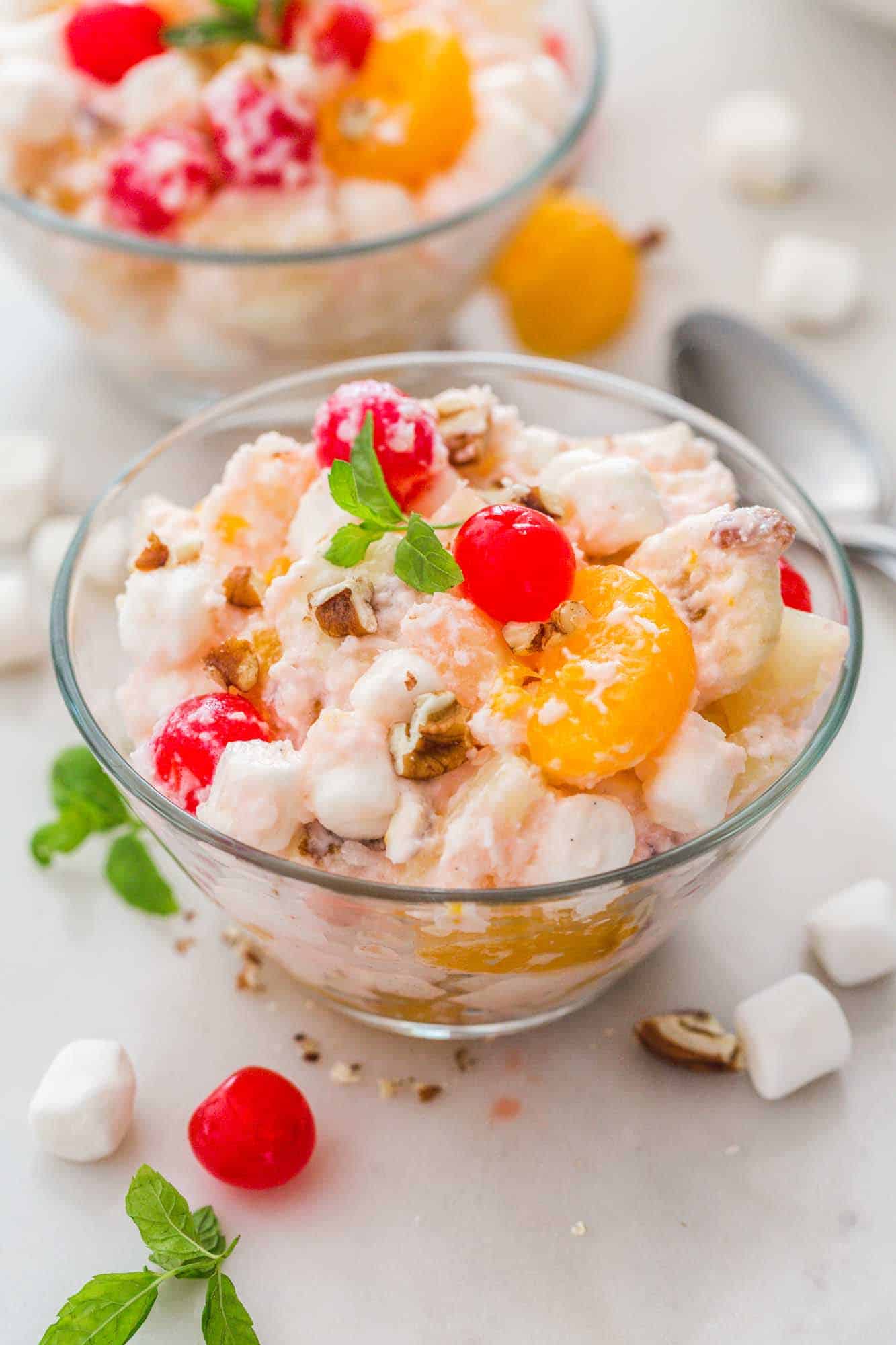 Ambrosia Salad served in glass bowls individual servings, garnished with mint leaves and maraschino cherries