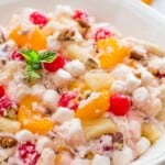 Large white plate with creamy ambrosia salad, and garnishes like fresh mint and chopped pecans