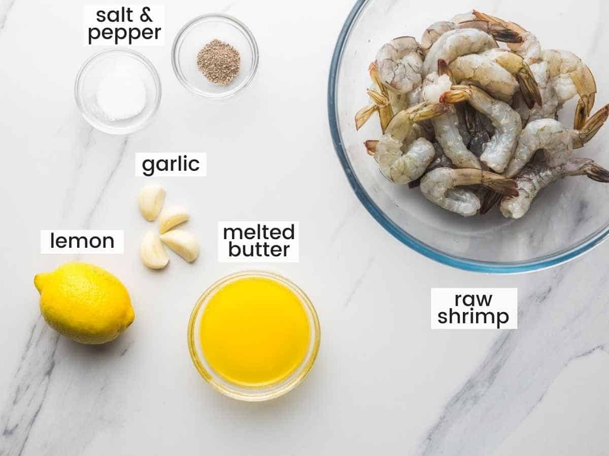 Ingredients needed for baked shrimp including raw shrimp, melted butter, lemon, garlic, salt and pepper.