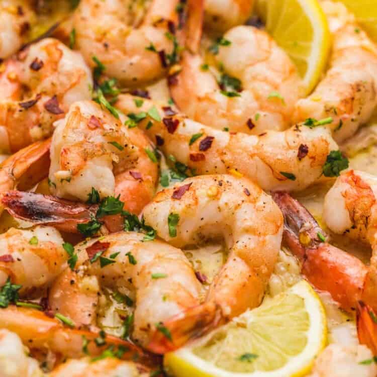 Close up shot of baked shrimp with lemon wedges and garnished with parsley and red pepper flakes