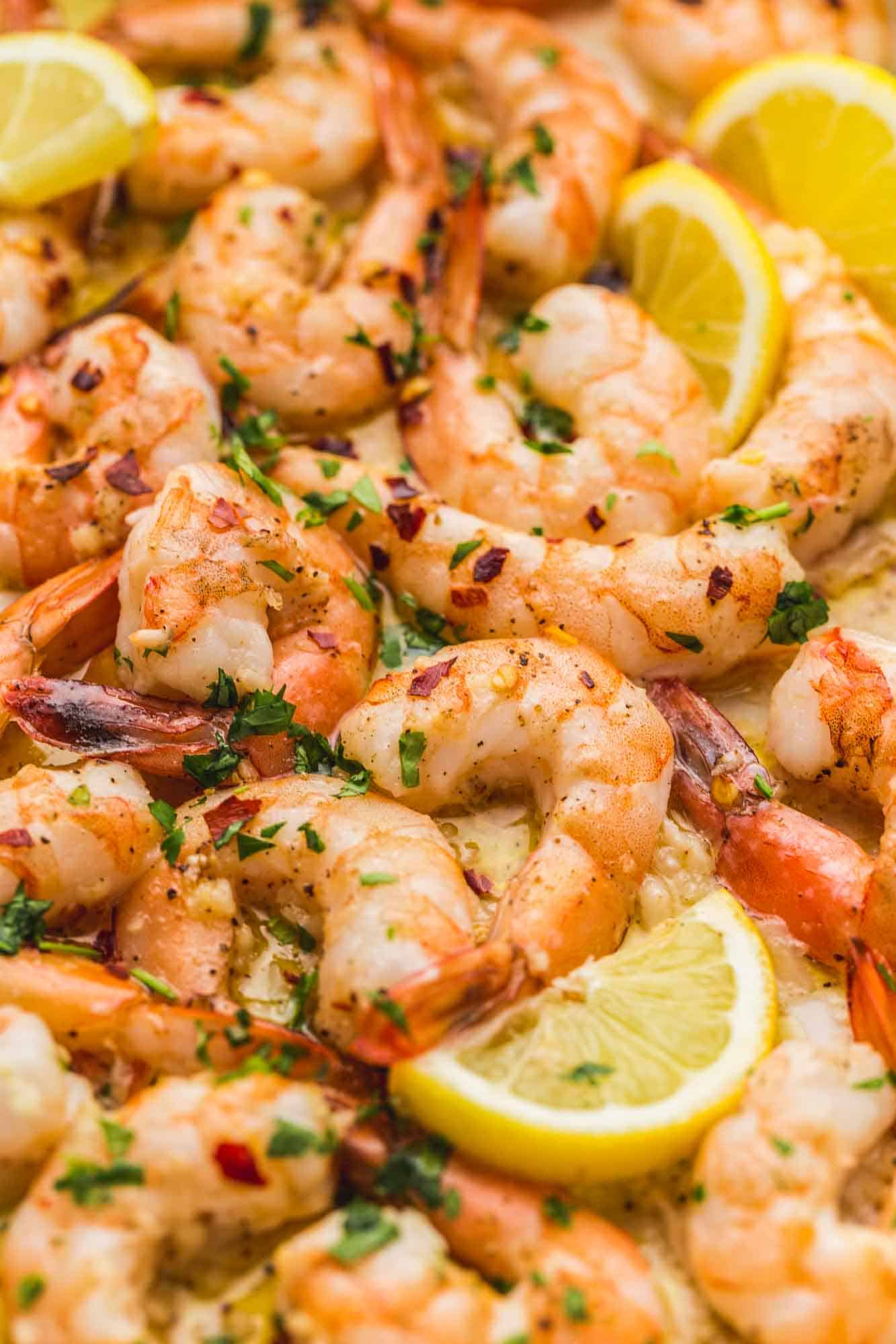 Close up shot of baked shrimp with lemon wedges and garnished with parsley and red pepper flakes