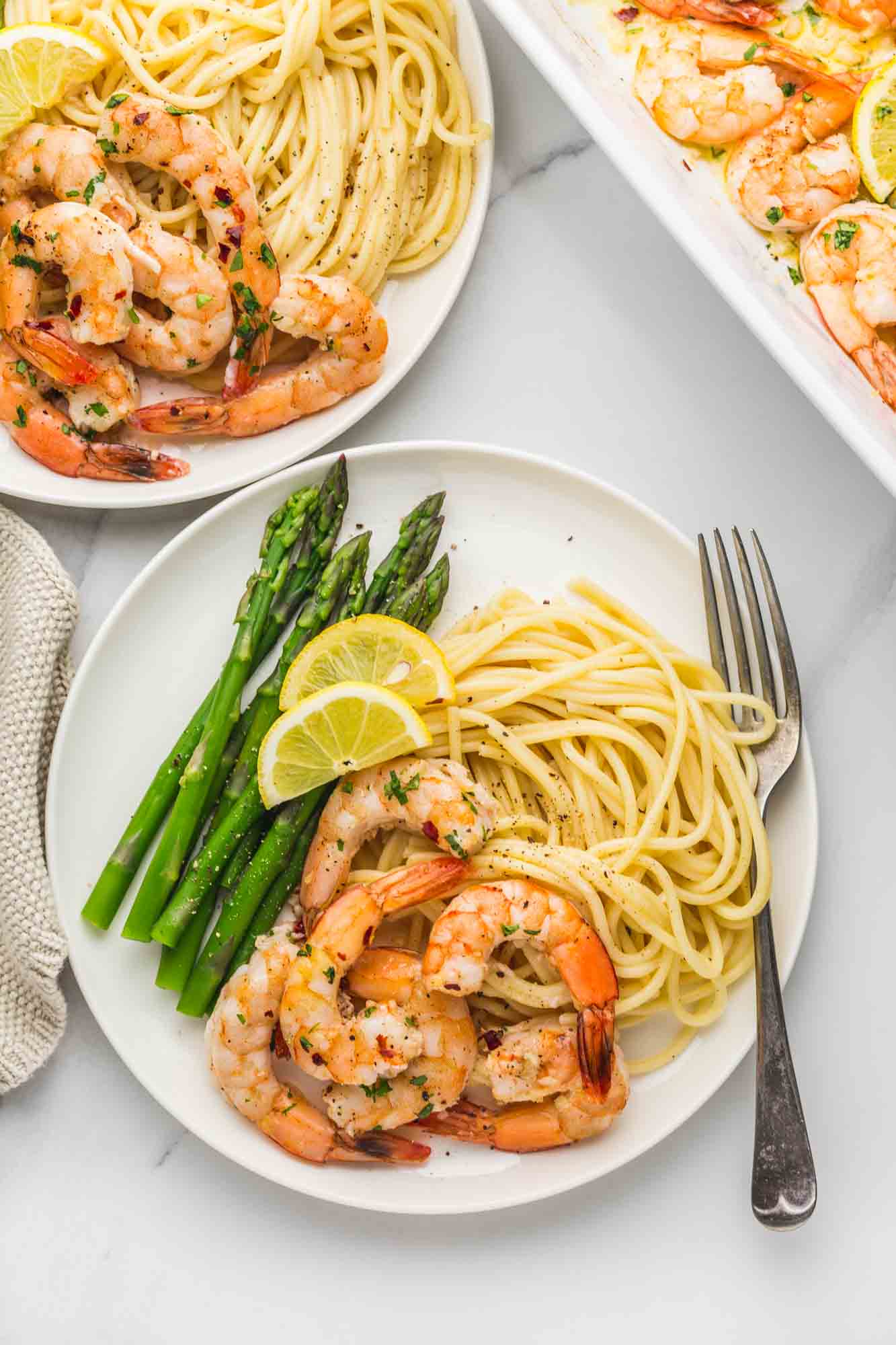 Bakeed shrimp served in two white plates with pasta and asparagus