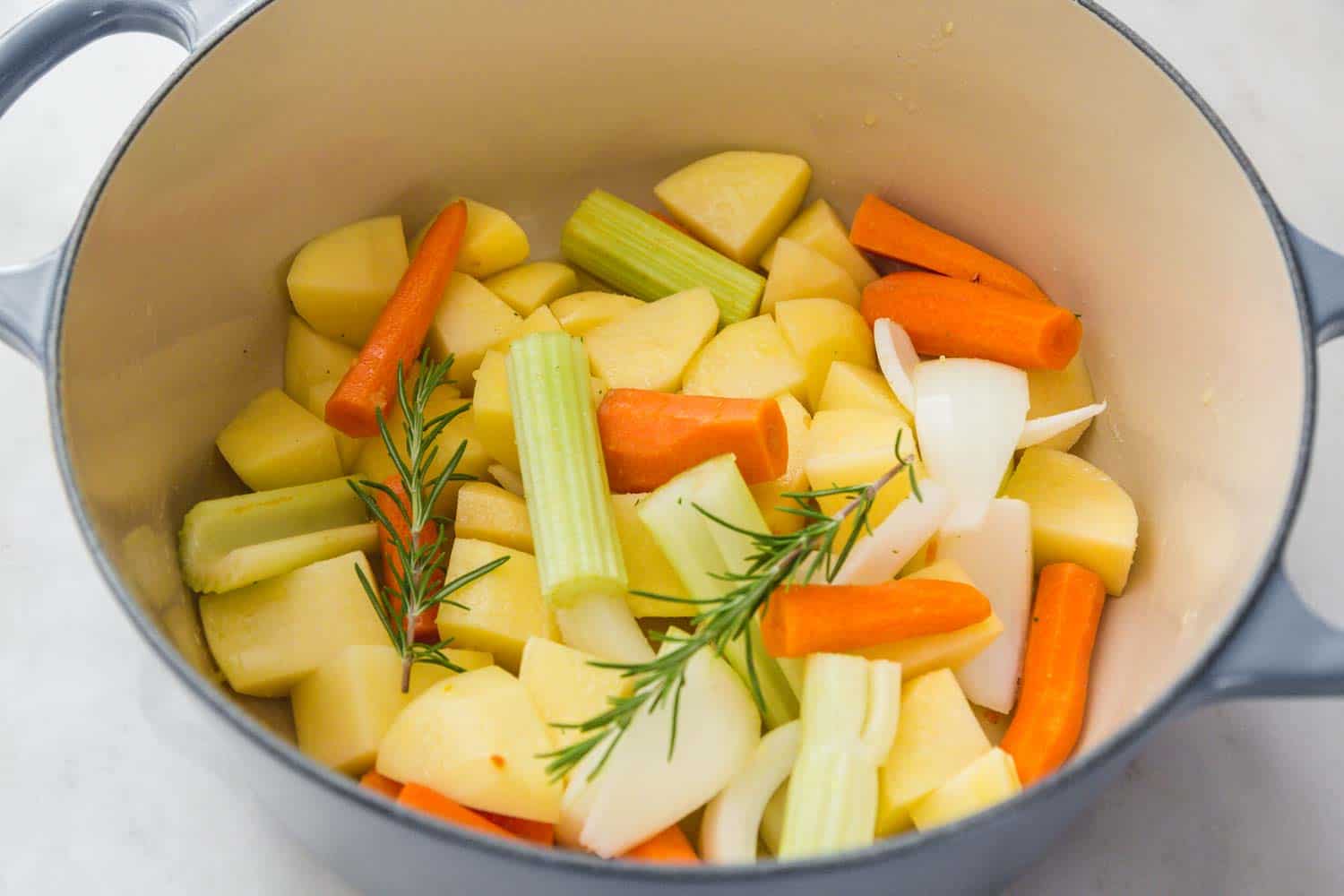 Vegetables including carrot, celery, onion and rosemary in a blue dutch oven