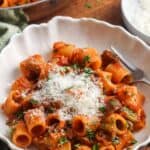 A white bowl filled with eggplant pasta topped with grated cheese and fresh parsley, with a fork on the side.