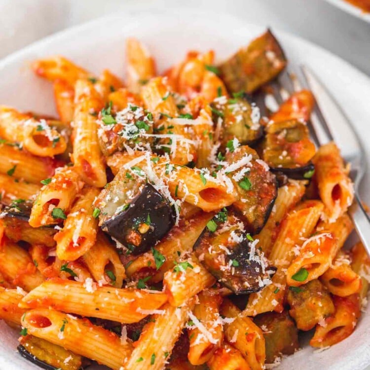 Eggplant pasta served in a white bowl and topped with parmesan cheese