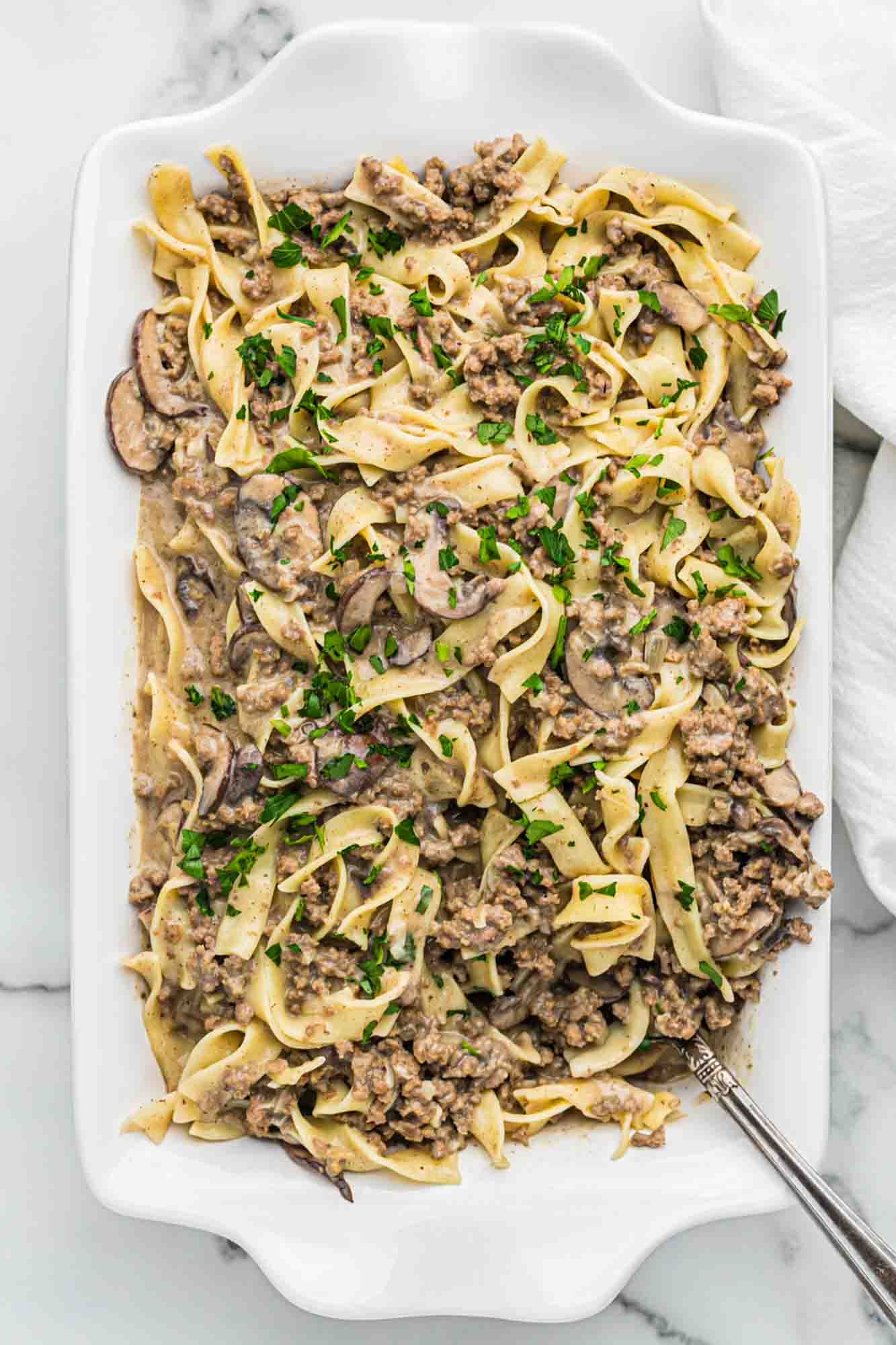 Overhead shot of ground beef stroganoff served in a white casserole dish, garnished with fresh parsley leaves