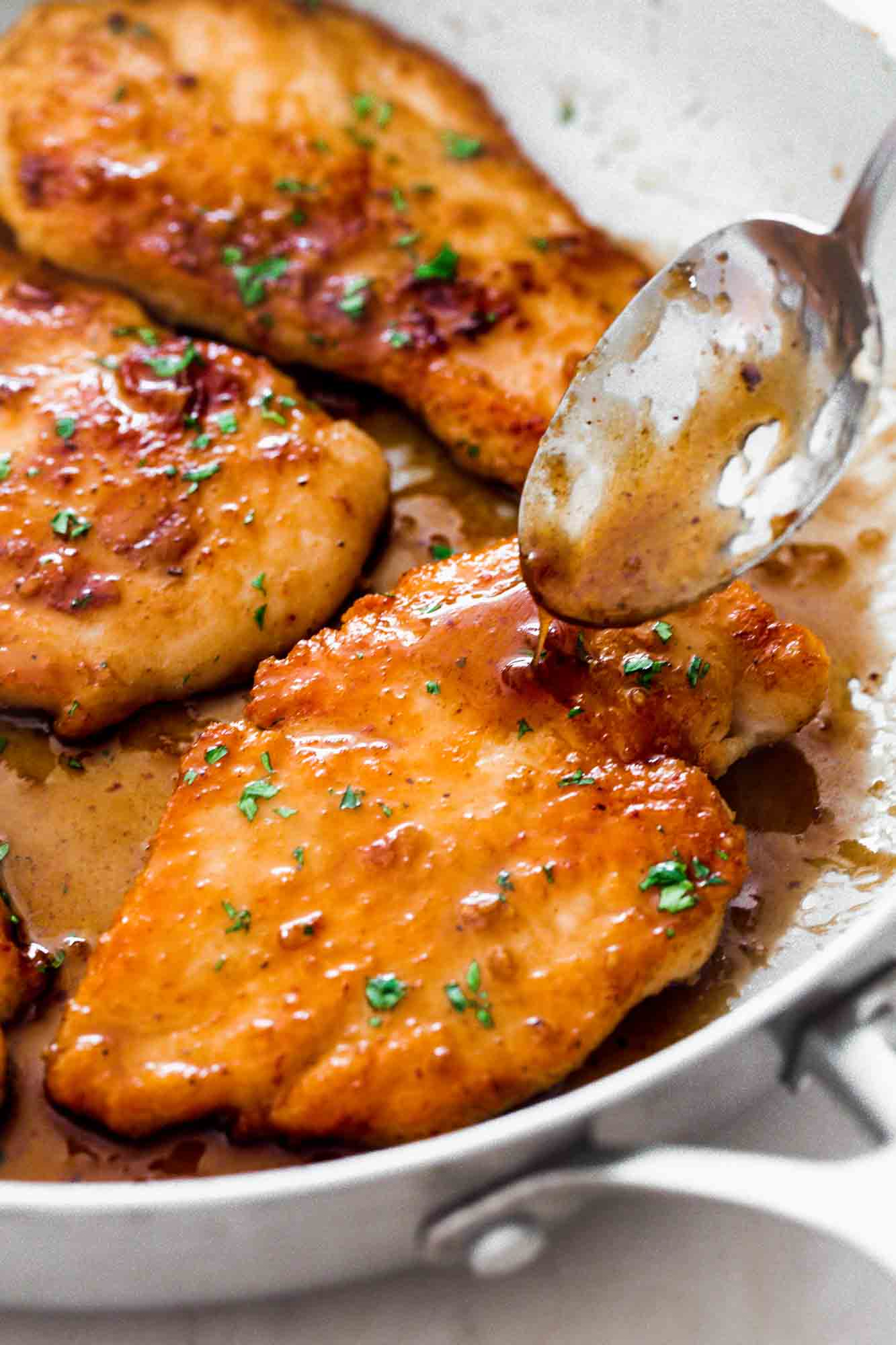 Spooning sauce over the honey garlic chicken cutlets in a pan