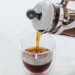 Pouring coffee from a french press into a double glass cup