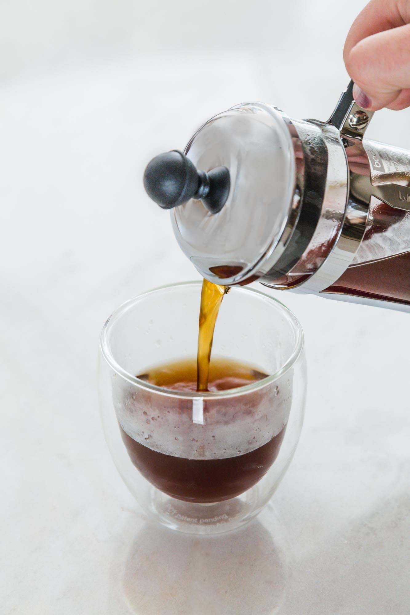 Pouring coffee from a french press into a double glass cup
