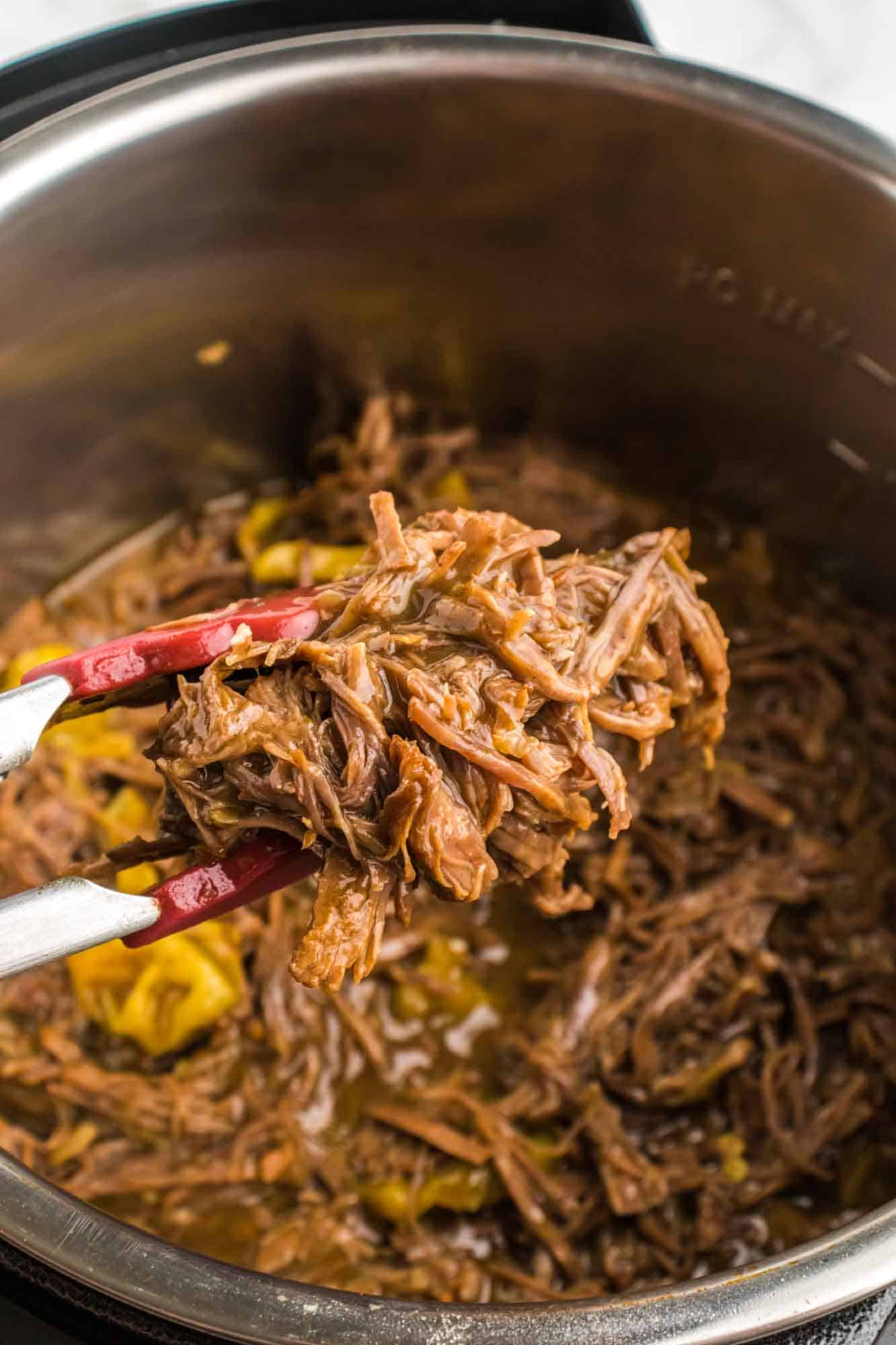 Taking shredded beef out of the Instant Pot using kitchen tongs