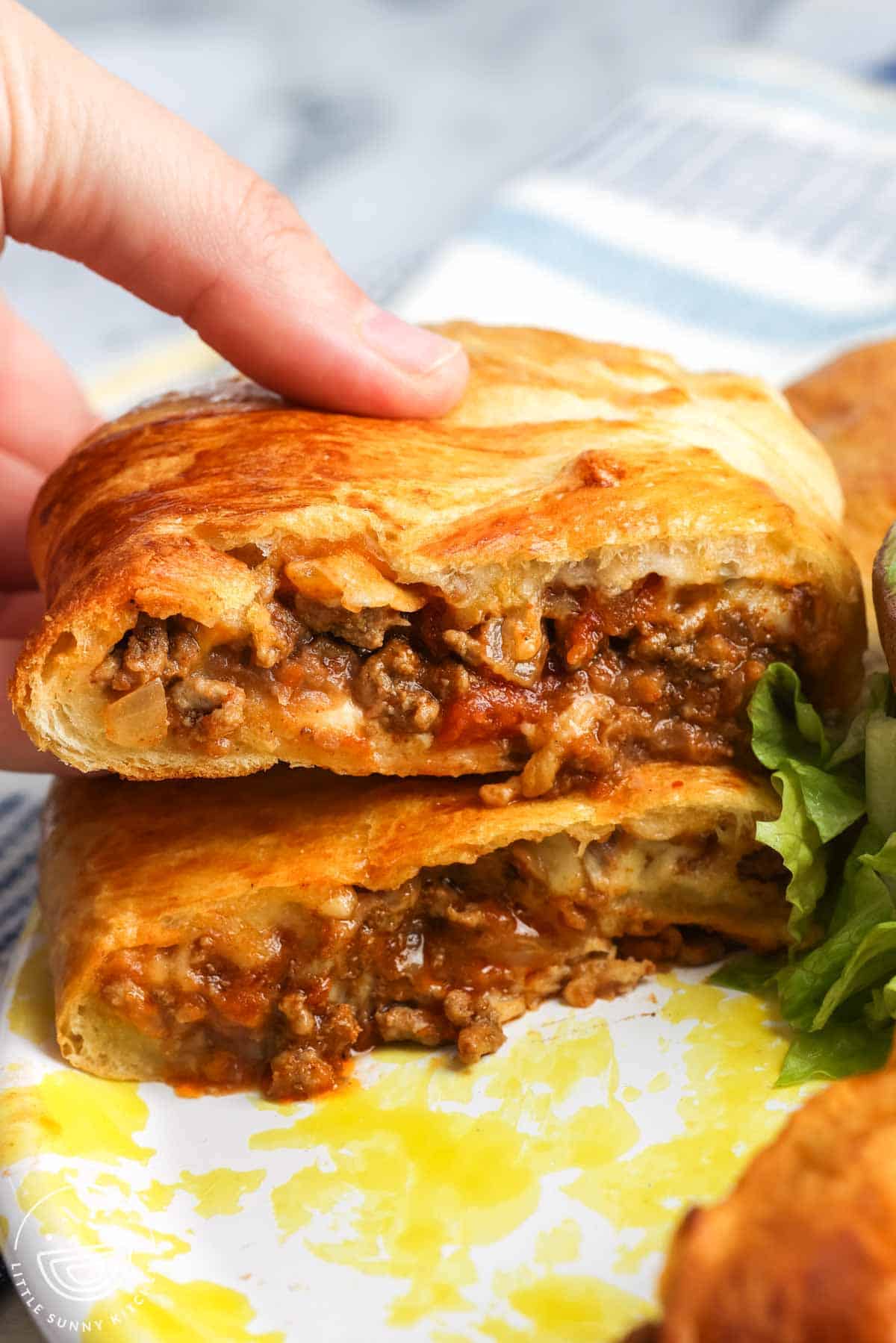 Close up of a sliced taco ring made with crescent roll dough, filled with seasoned ground beef, melted cheese, and onions, showing the flaky golden crust and savory filling on a plate with lettuce on the side