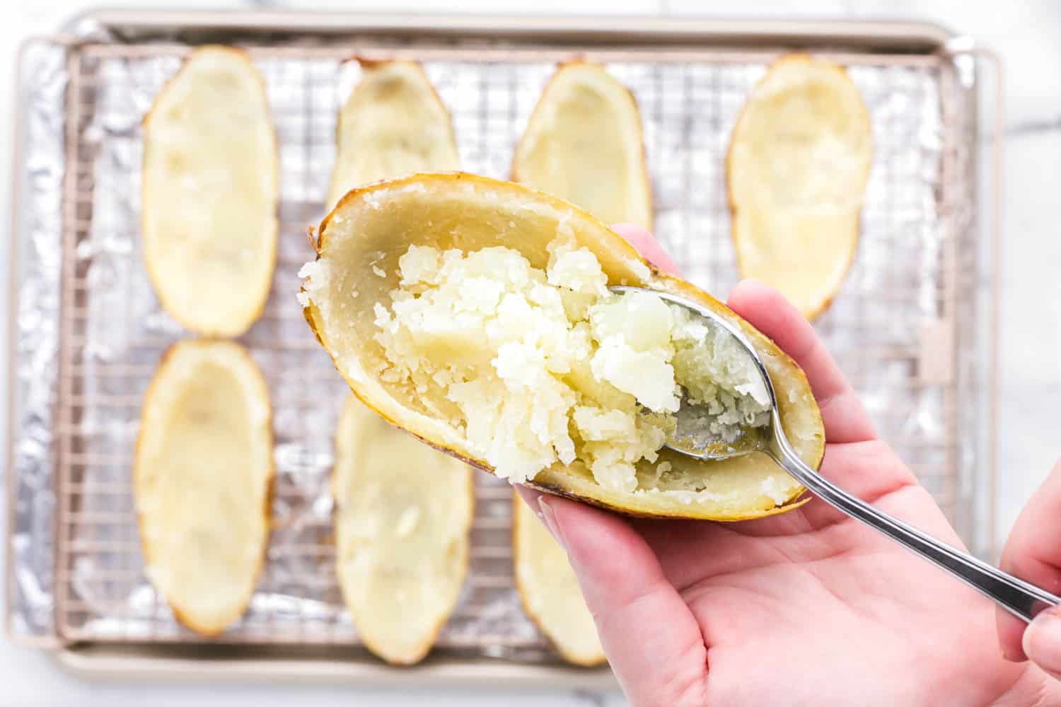 Scooping out potato flesh from each baked potato half