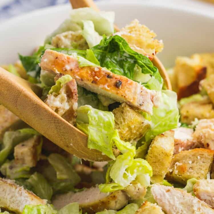 Serving chicken caesar salad with wooden serving spoons