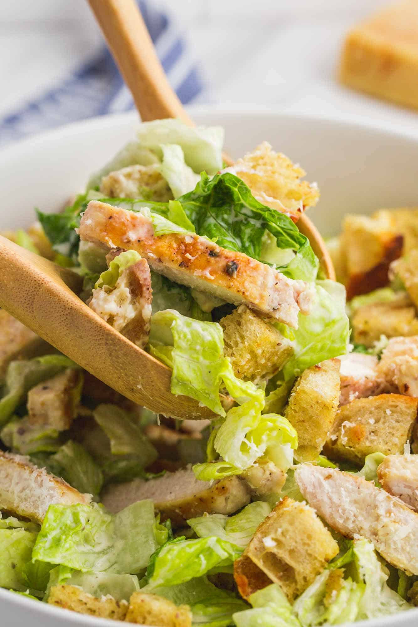 Serving chicken caesar salad with wooden serving spoons