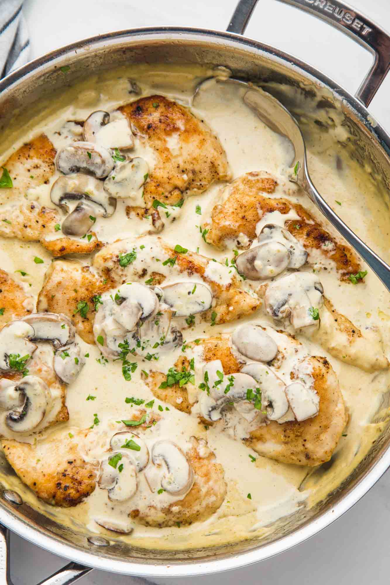 Creamy mushroom chicken in a skillet garnished with parsley in a stainless steel skillet