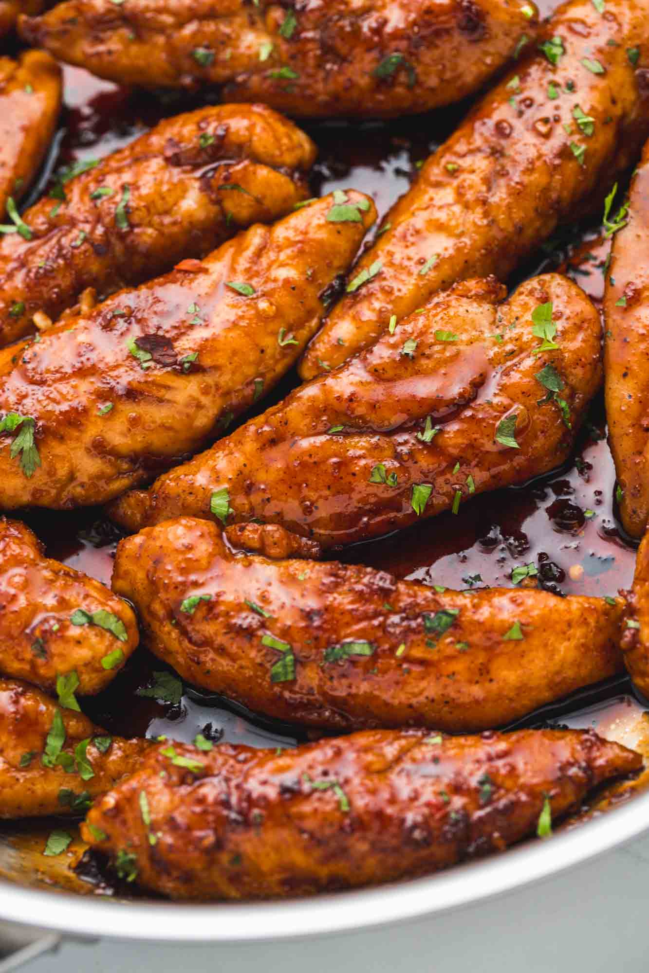 Close up shot of honey garlic chicken tenders in a stainless steel skillet