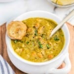 Split pea soup in a white bowl with toasted crusty bread and a spoon