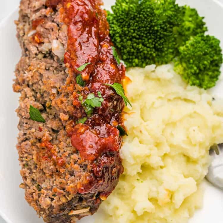 Slice of meatloaf served on a white plate with mashed potatoes and steamed broccoli
