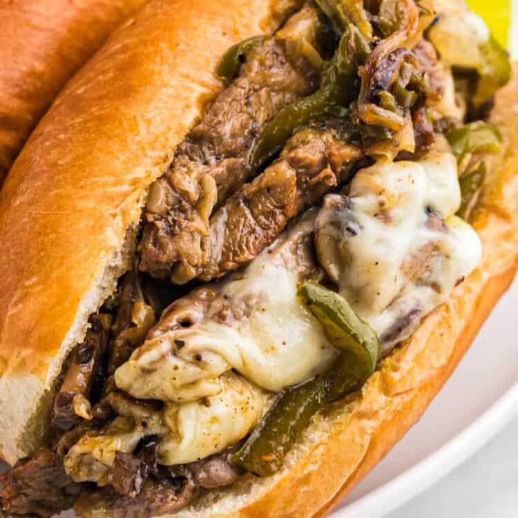Philly cheesesteak sandwich on a white plate served with sweet pickles