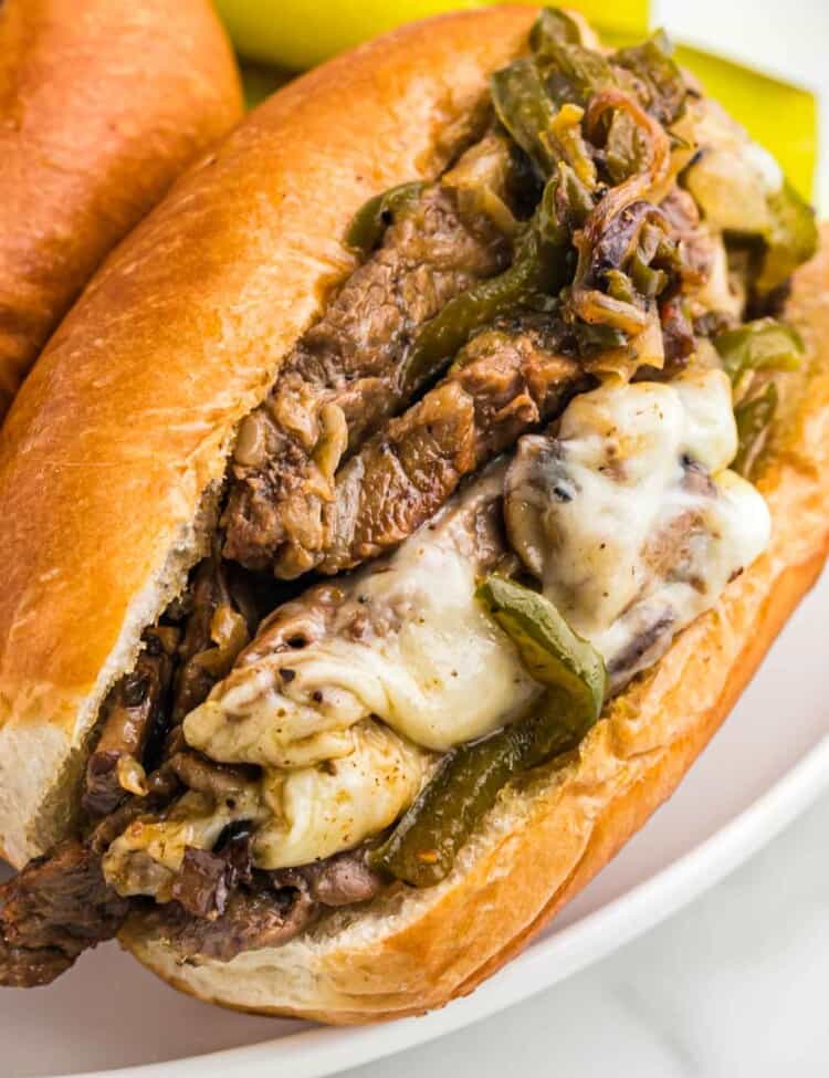 Philly cheesesteak sandwich on a white plate served with sweet pickles