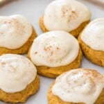 Pumpkin cookies frosted with cream cheese frosting served on a white plate, placed on a wire rack