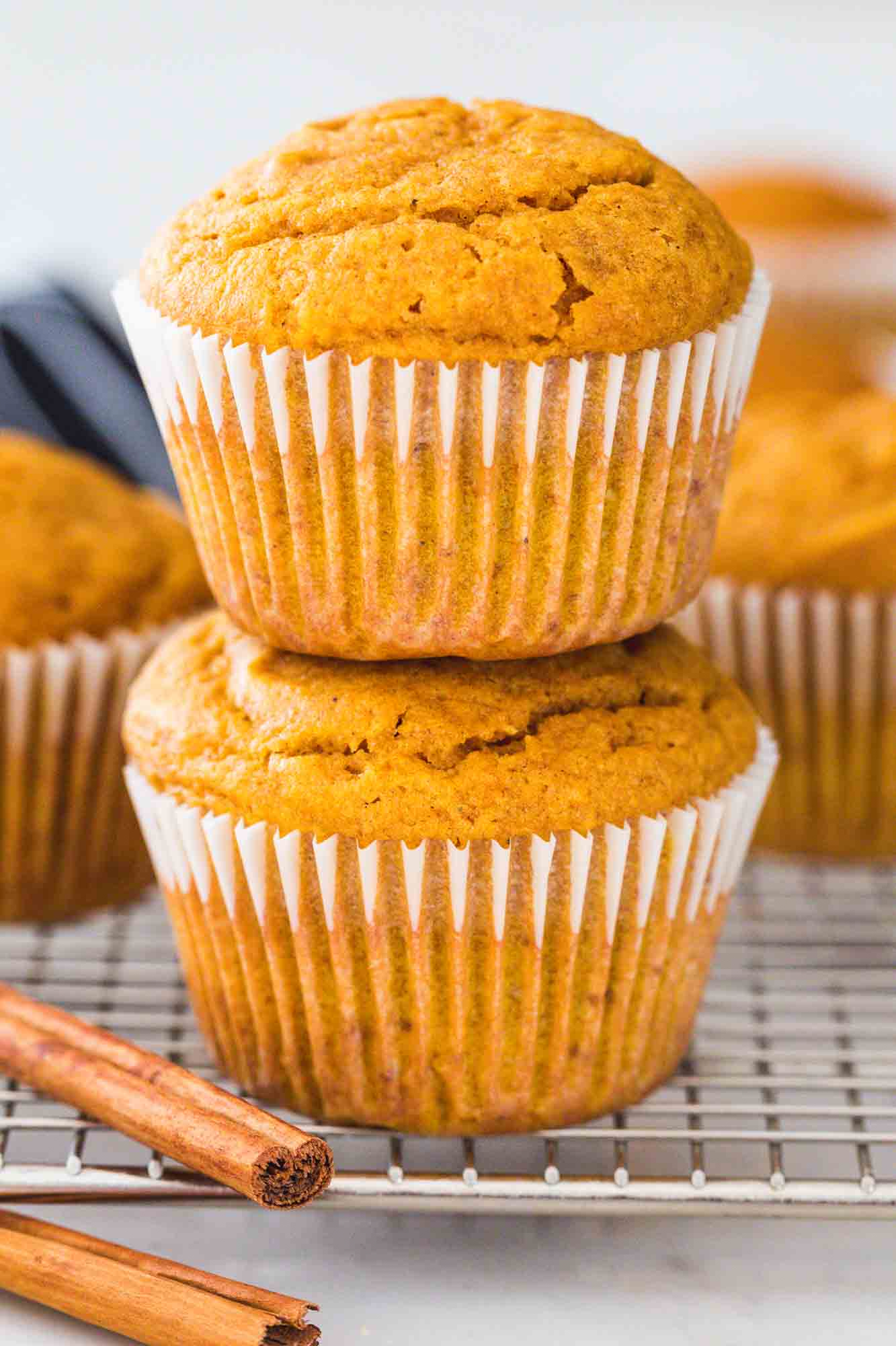 Two pumpkin muffins stacked on a wire rack, and cinnamon sticks on the side