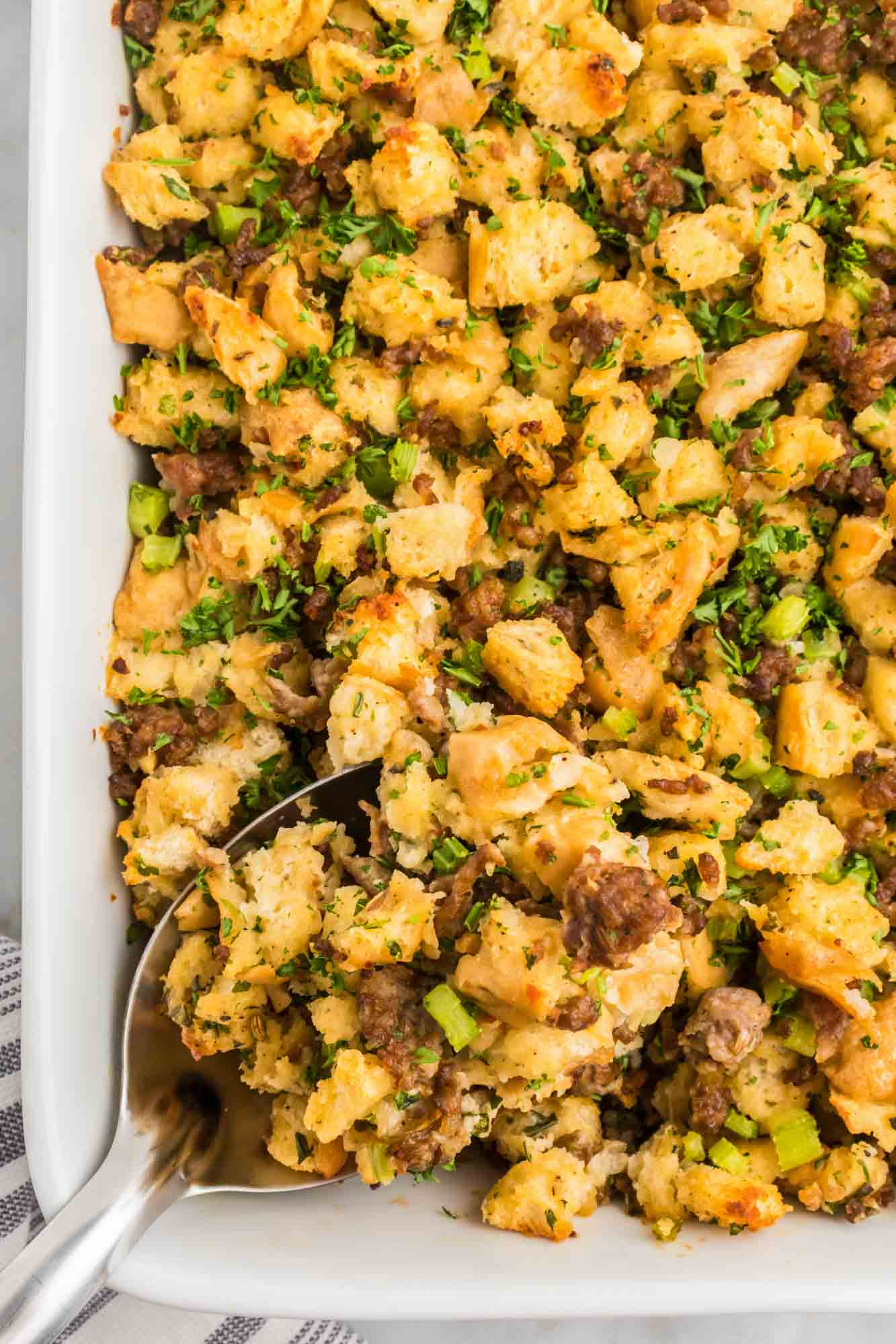 Overhead shot of sausage stuffing in a baking dish with a serving spoon