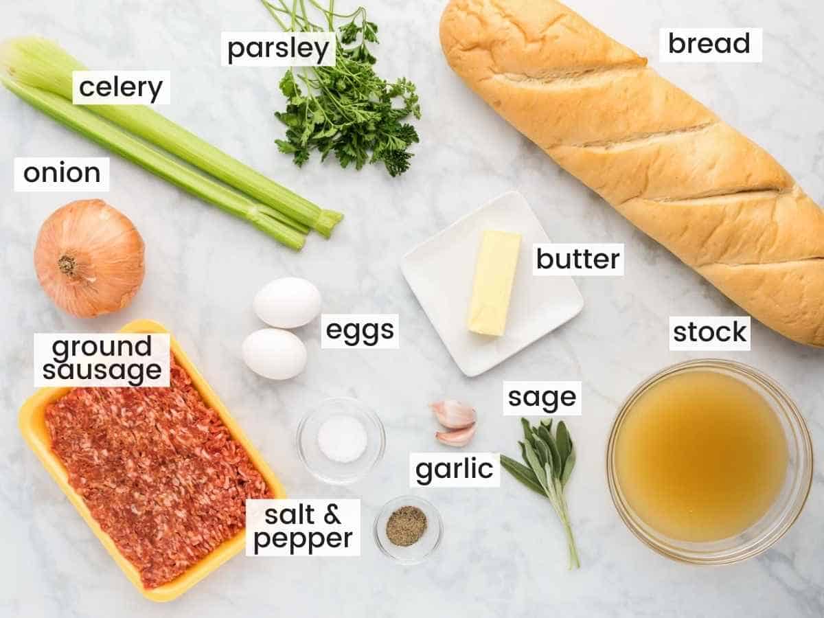 Ingredients needed to make sausage stuffing including bread, sausage, celery, onion, garlic, parsley, stock, eggs, sage and butter.