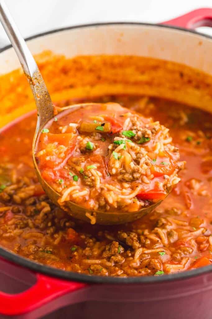 Ladle full of stuffed pepper soup and soup in a red dutch oven