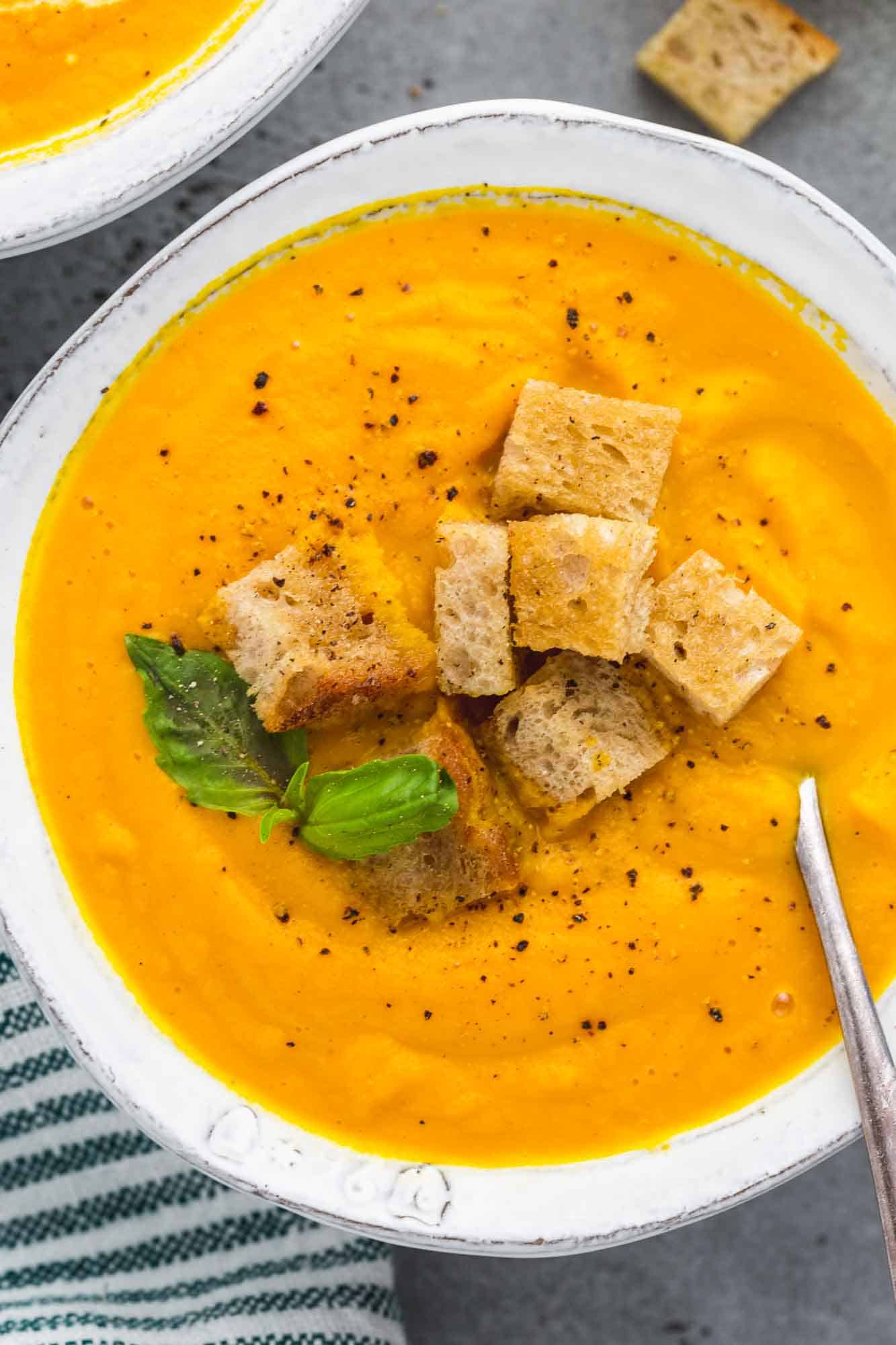 Creamy roasted carrot soup in a white bowl served with homemade croutons and basil leaves
