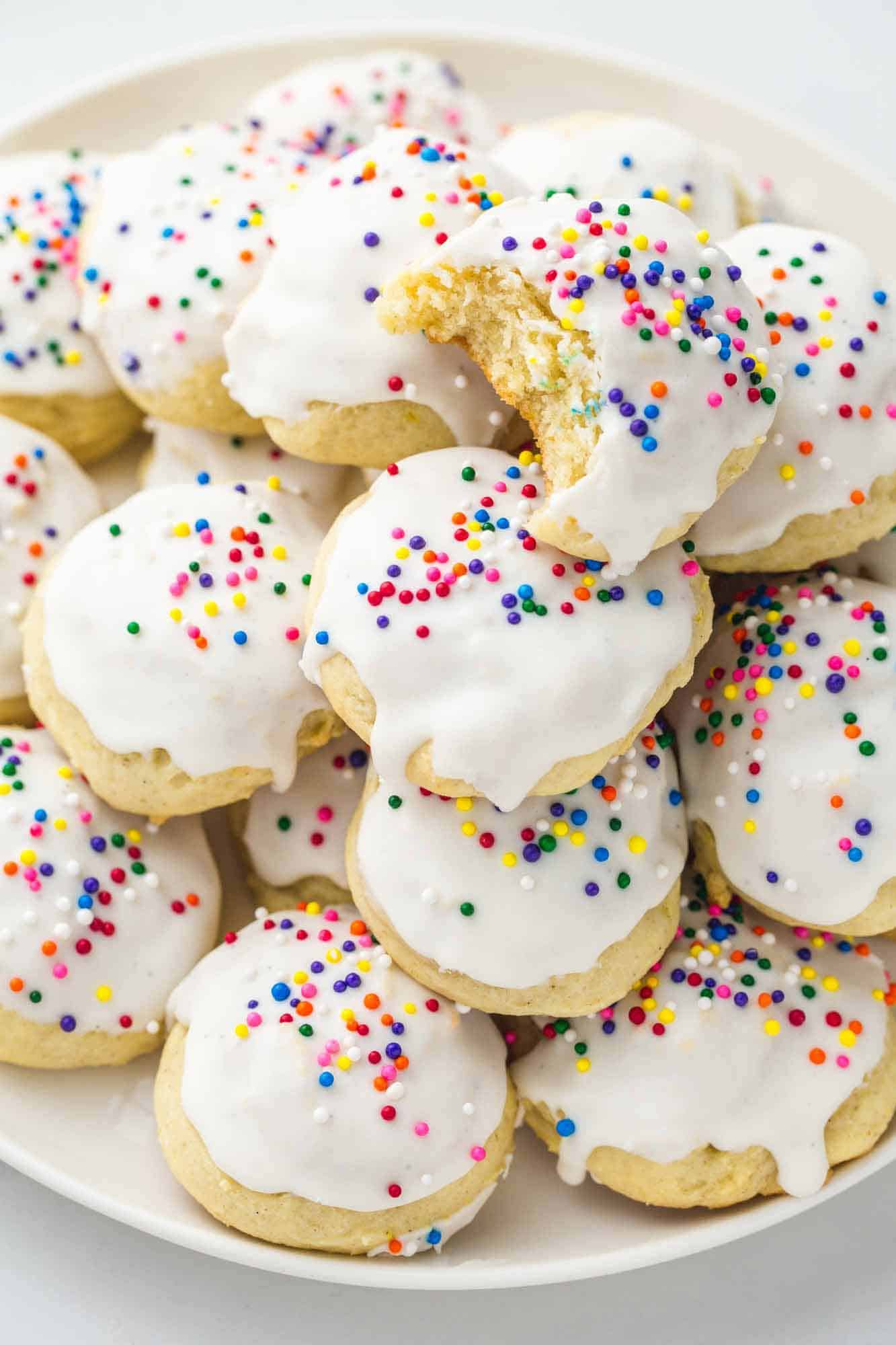 Stacked ricotta cookies on a white plate, decorated with vanilla glaze and colorful sprinkles.