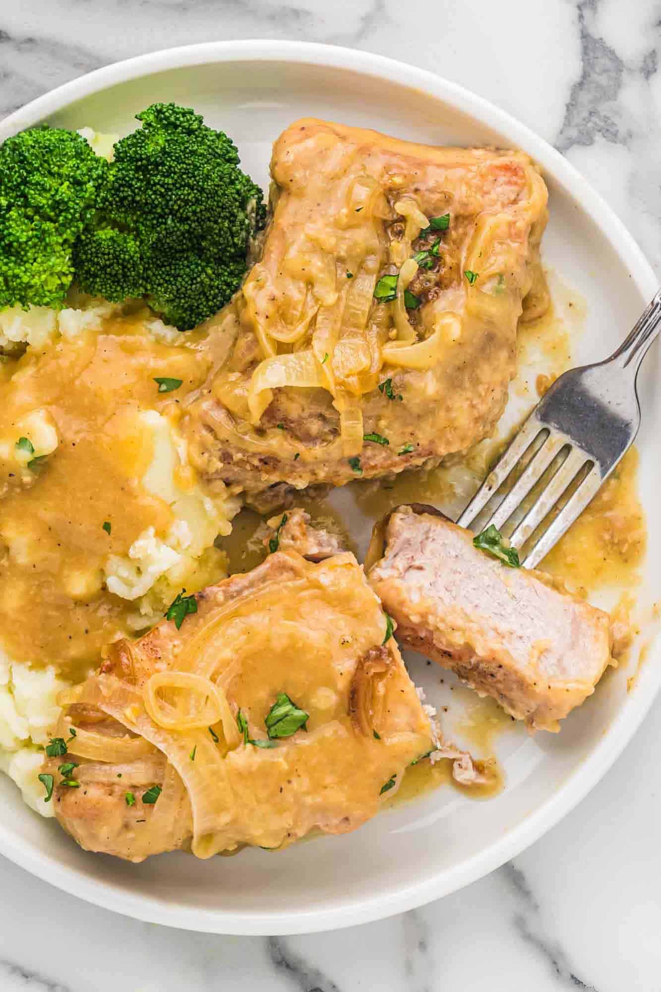 Slow cooker pork chops in a white plate served with mashed potatoes and broccoli