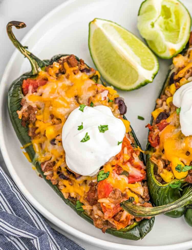 Stuffed poblano pepper on a plate with sour cream, and lime wedges.