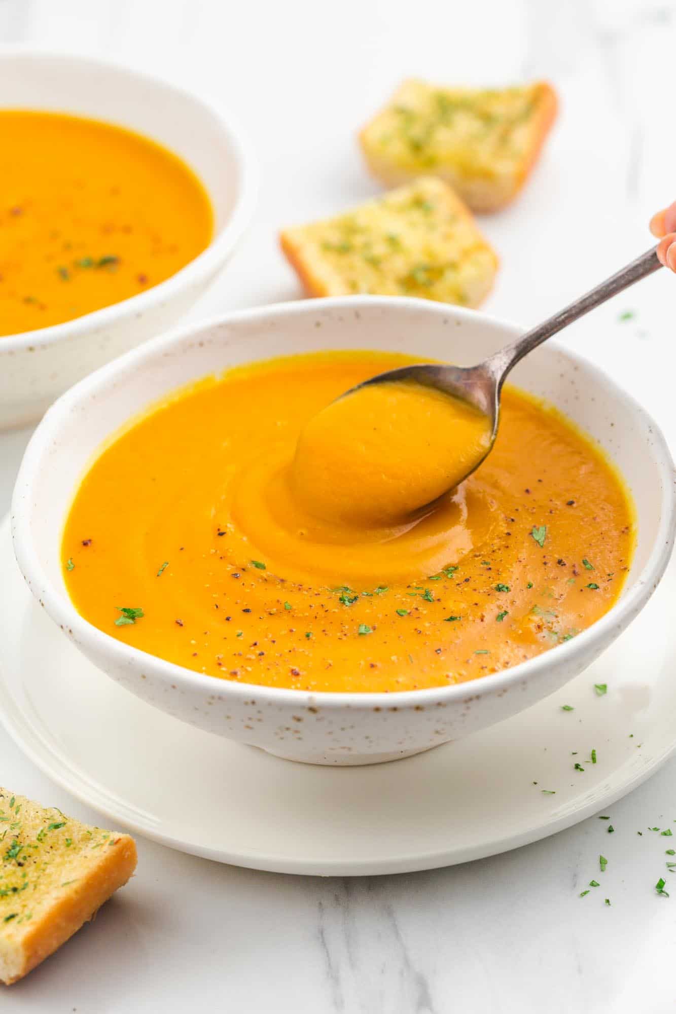 Taking a spoonful of the sweet potato soup in a white bowl