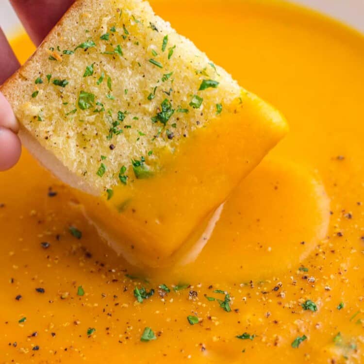 dipping garlic bread in a bowl of sweet potato soup