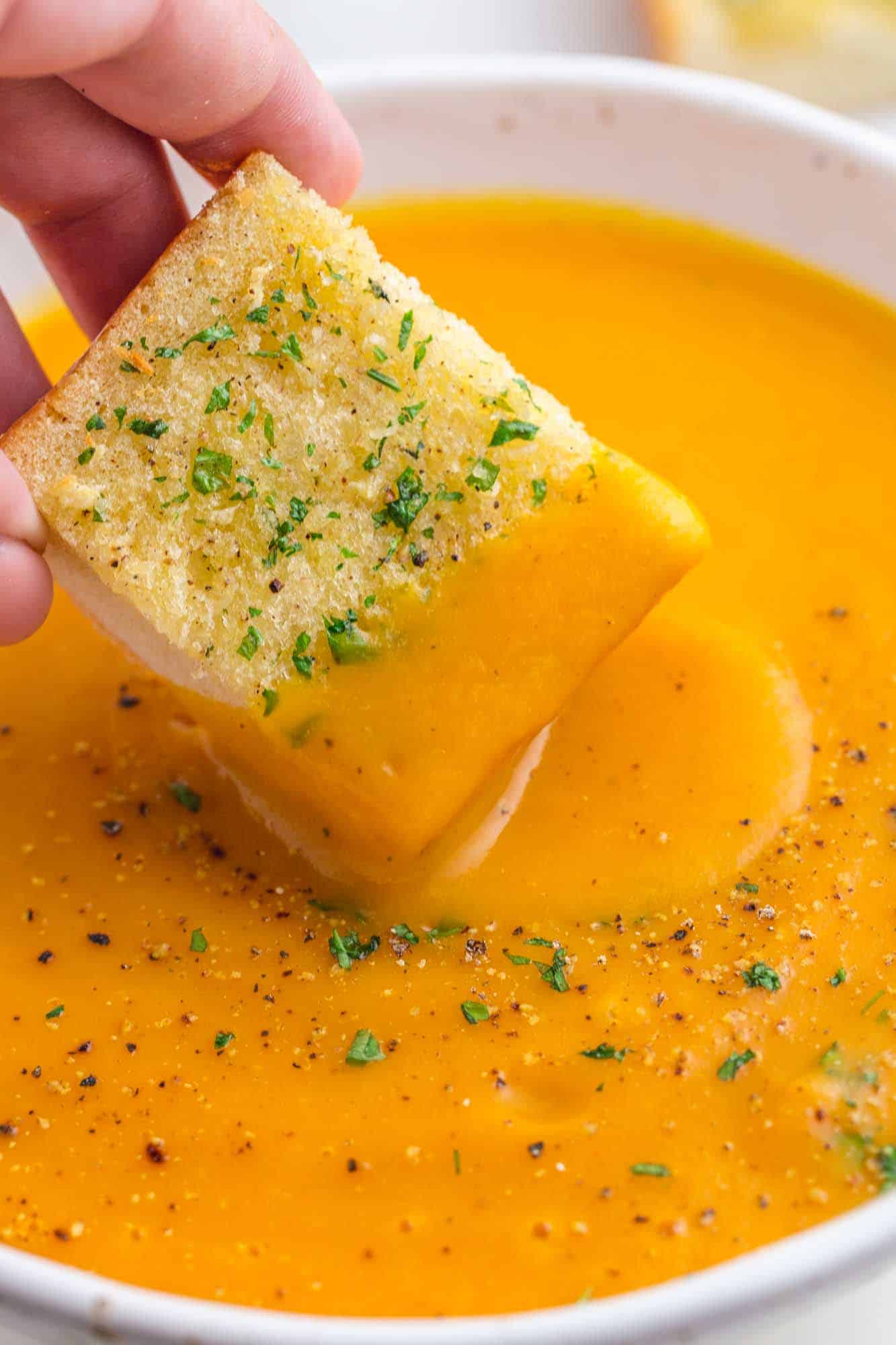 dipping garlic bread in a bowl of sweet potato soup
