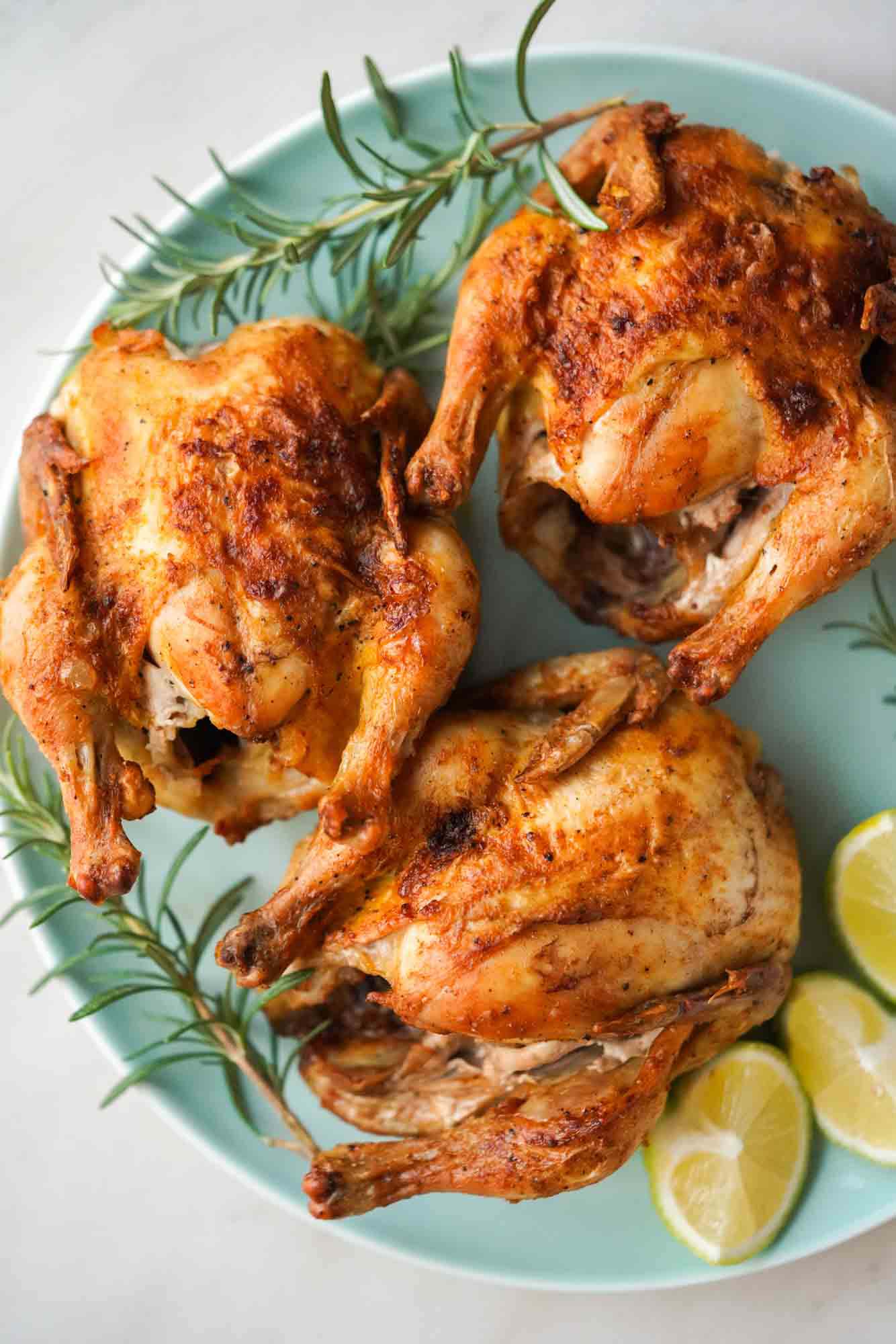 Air fried cornish hens served on a plate with fresh lemon wedges and rosemary