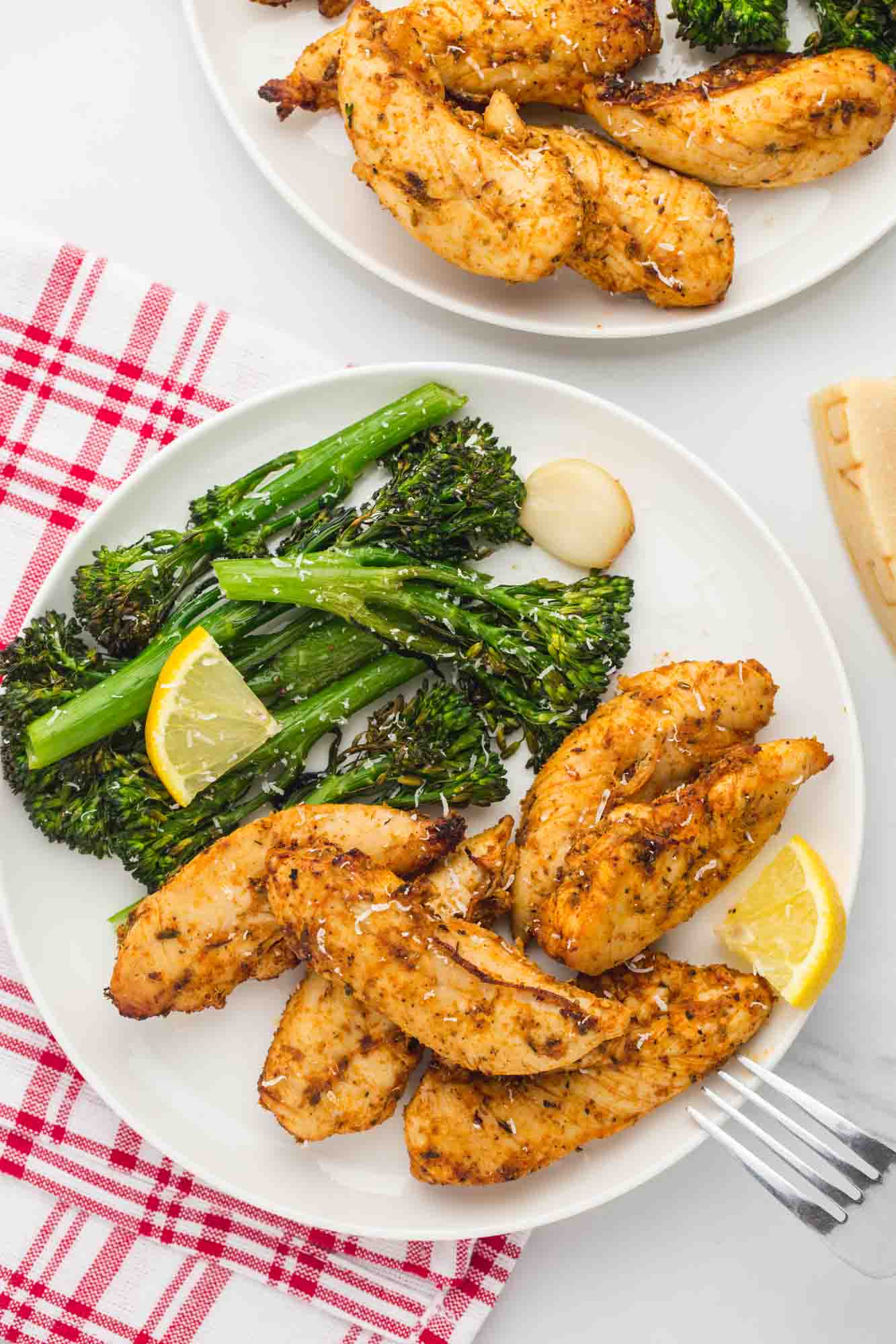 Overhead shot of 2 white plates with grilled chicken tenders and roasted broccolini