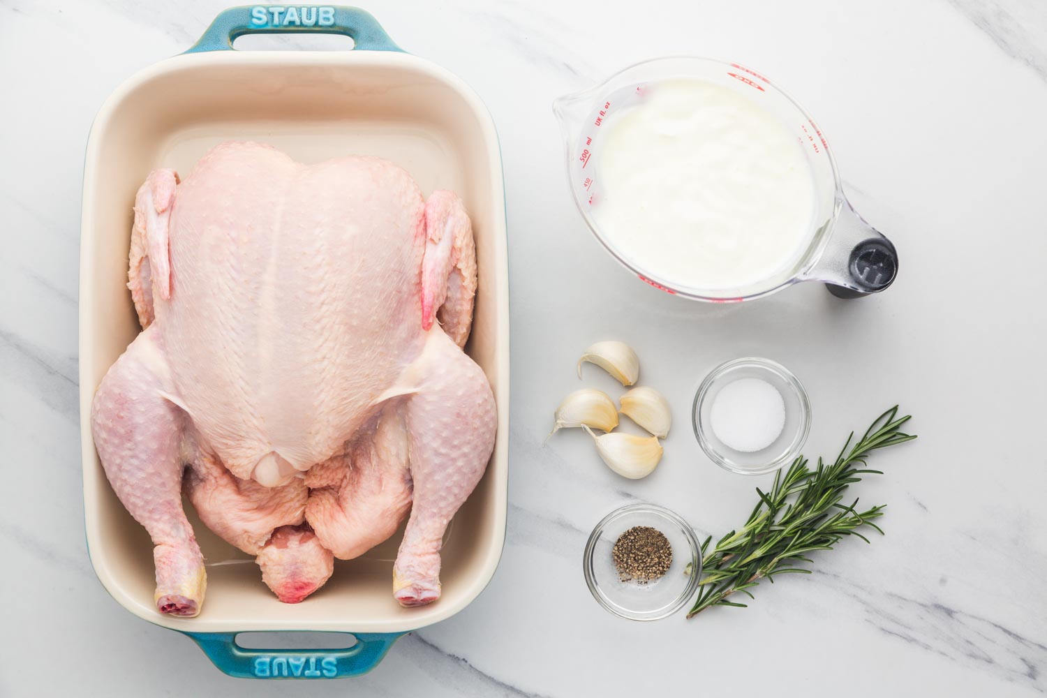 Ingredients needed to marinate a chicken in buttermilk including a whole chicken, buttermilk, garlic, rosemary, salt and pepper.