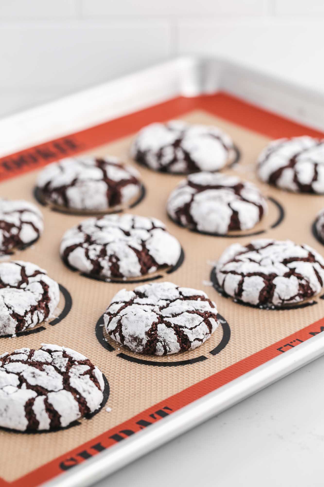 Chocolate crinkle cookies on a cookie sheet lined with Silpat mat