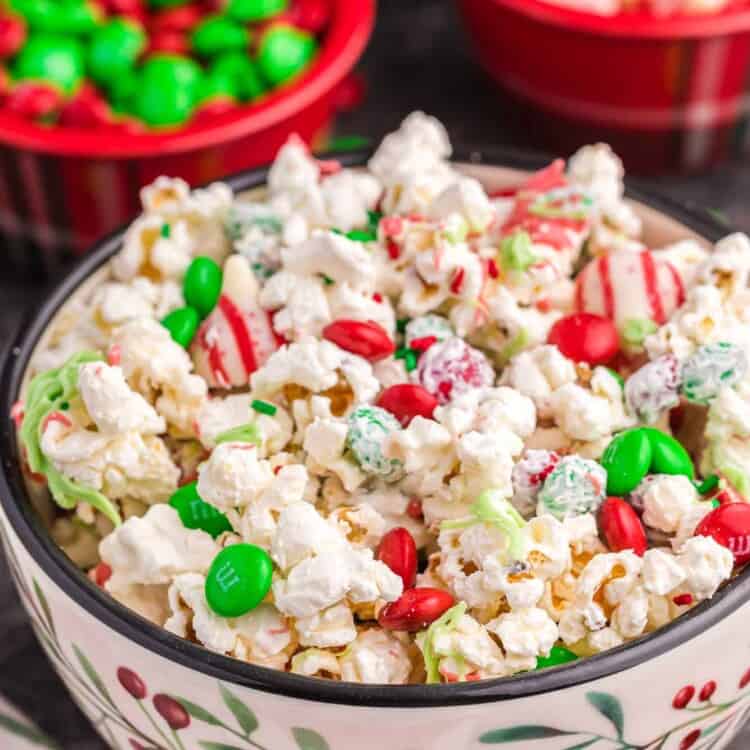 Christmas popcorn served in a festive bowl, with holiday M&Ms and candy cane hersheys in the background.