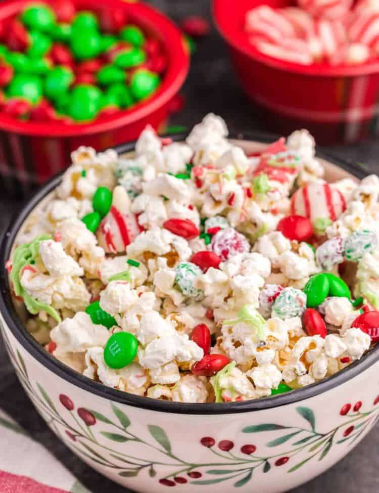 Christmas popcorn served in a festive bowl, with holiday M&Ms and candy cane hersheys in the background.
