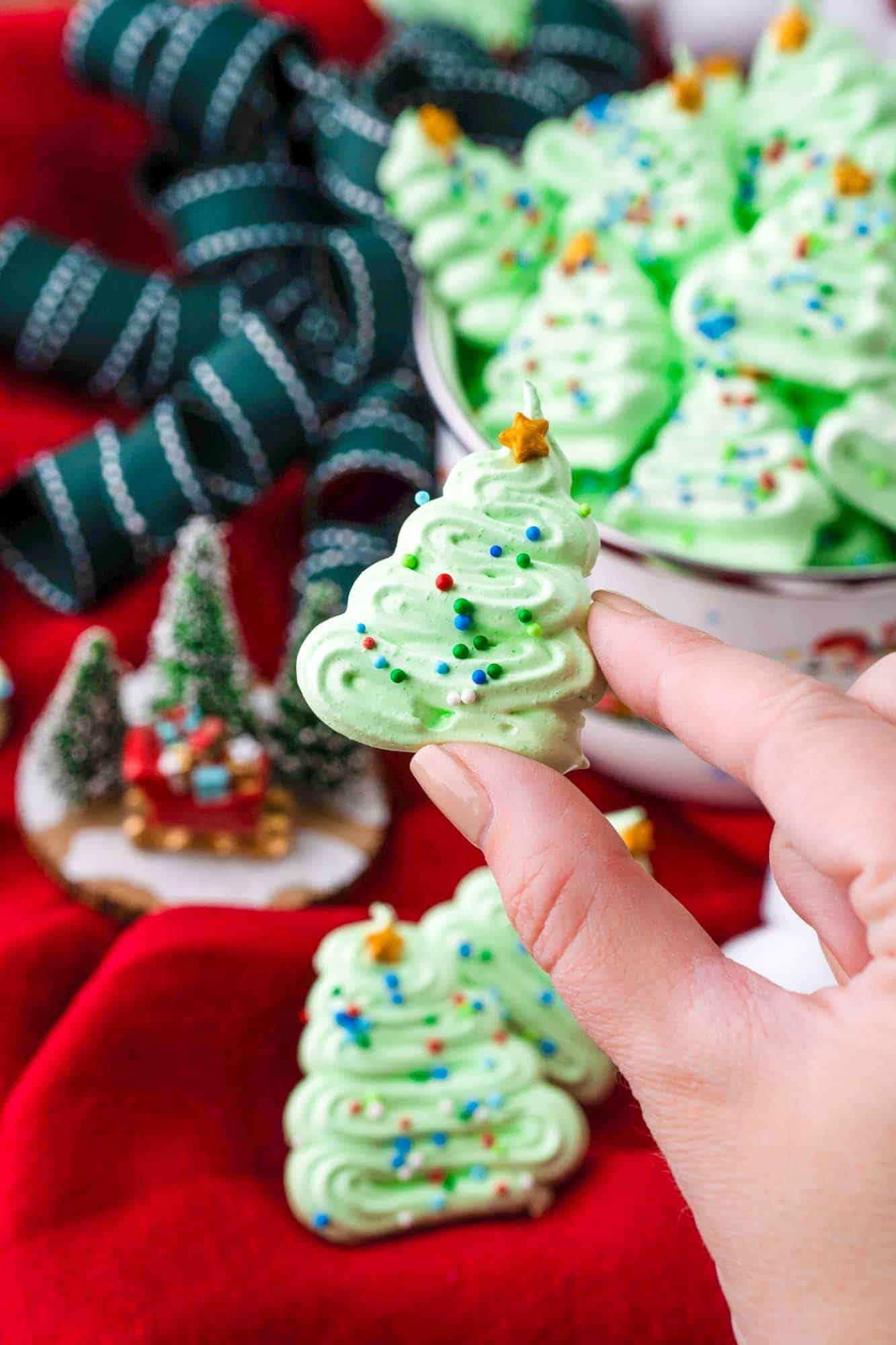Holding a meringue cookie shaped like a Christmas tree and decorated with sprinkles