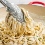Taking a portion of super creamy Cream Cheese Pasta Sauce from the pan using kitchen tongs