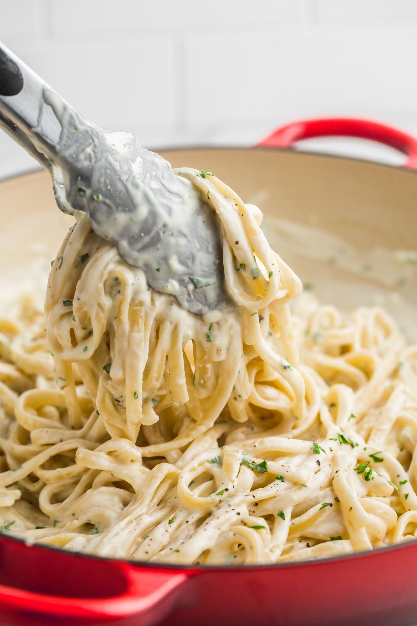 Taking a portion of super creamy Cream Cheese Pasta Sauce from the pan using kitchen tongs