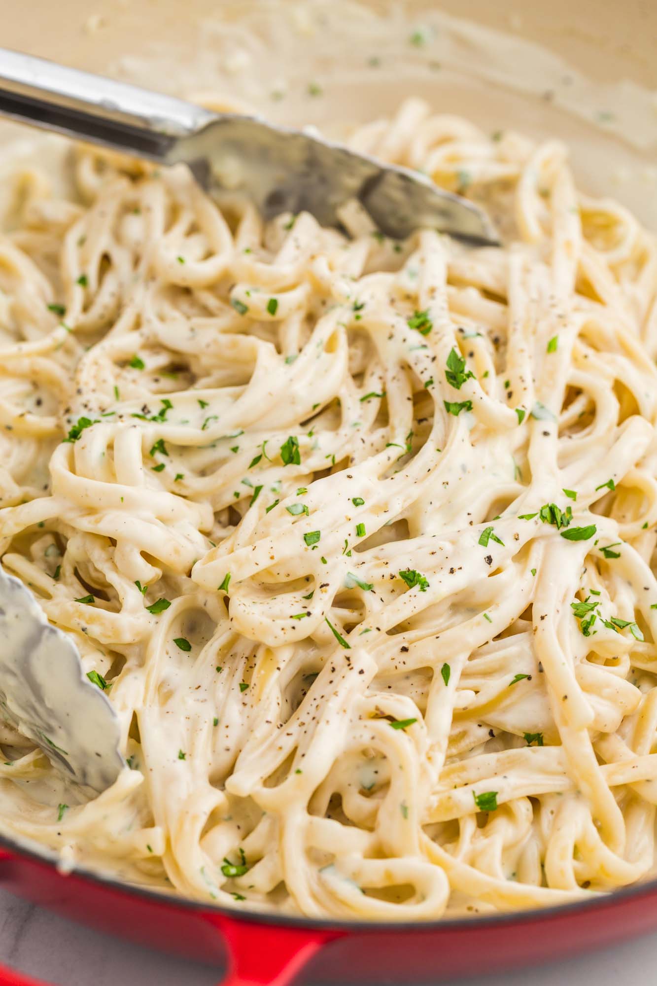 Creamy cream cheese pasta in a shallow pan with kitchen tongs