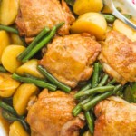 Glazed honey garlic chicken thighs served on a white platter with baby potatoes and green beans, overhead shot.